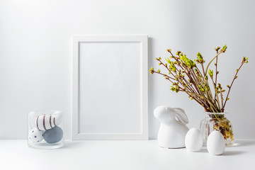 Wall Mural - Home interior with easter decor. Mockup with a white frame and green buds on branches in a vase on a light background