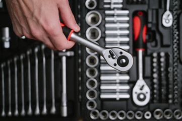 human auto mechanic hand holding car repair tool socket wrench on tool box kit background