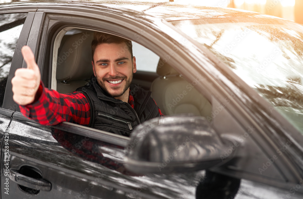 Young attractive Caucasian man sits at the wheel of his car sunny winter day.