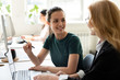 © fizkes - Smiling millennial female employee sit at desk talk with woman colleague coworker, happy confident businesswomen brainstorm cooperate working at laptop in office together, collaboration concept