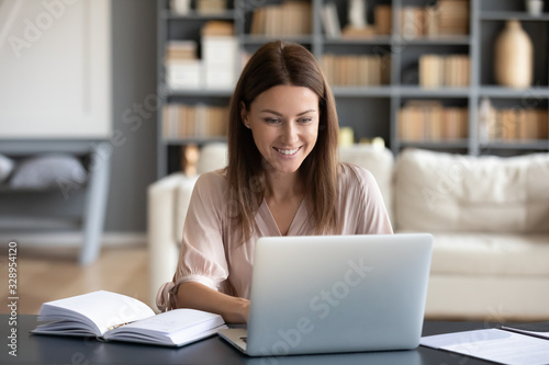 Photographie Head shot young happy woman sitting at desk, working on computer at home