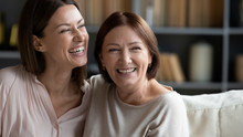 Head Shot Close Up Happy Young Woman Hugging Mature Brunette Mother, Feeling Excited About Positive News At Home. Smiling Two Female Generation Family Dreaming Of Future Together, Resting On Sofa.