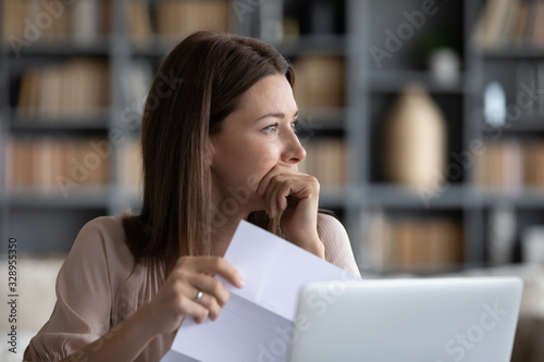 Fotografía Head shot stressed young woman holding paper document, bank debt notification, thinking of financial troubles, looking away
