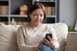 © fizkes - Pleasant senior older lady resting on couch, using applications on smartphone. Happy old mature woman chatting in messenger or social network with friends or children, shopping in internet store.