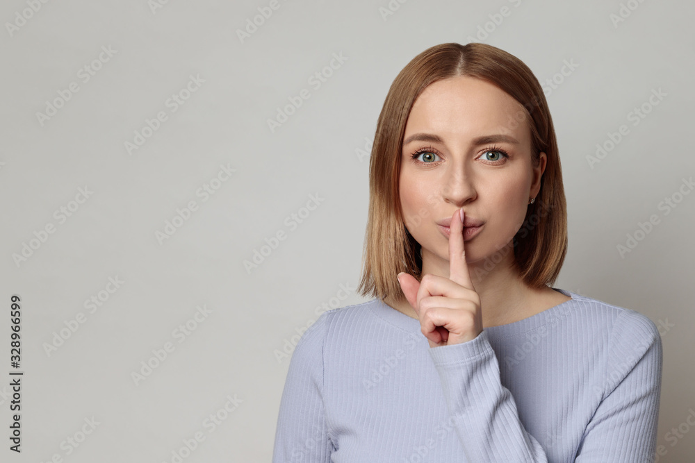 Shhh! European mysterious woman with short hair keep index finger over lips gesturing silence, isolated over grey background with copy space. Keep quiet, hush, privacy concept.  - obrazy, fototapety, plakaty 