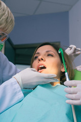 Wall Mural - Female dentist in dental office examines the mouth and teeth of a female patient