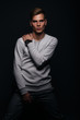 © qunica.com - Informally ( casual ) dressed blonde young man with sharp jawline in his 20's posing in a studio in front of a black background while wearing a white sweater.