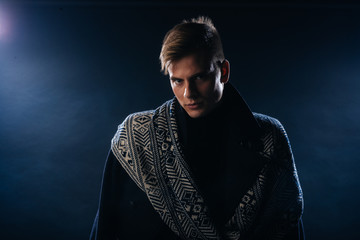 Canvas Print - Portrait of a handsome with sharp jawline young man wearing a scarf while posing inside a studio on a black background..