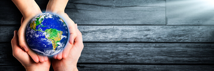 caring hands of man and woman holding earth on wooden background - earth day / care for the environm