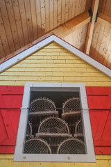 Indoor display of lobster or crab traps inside a window with red shutters, on a yellow clapboard wall.