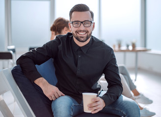 Poster - young businessman with a Cup of coffee sitting in a modern office.