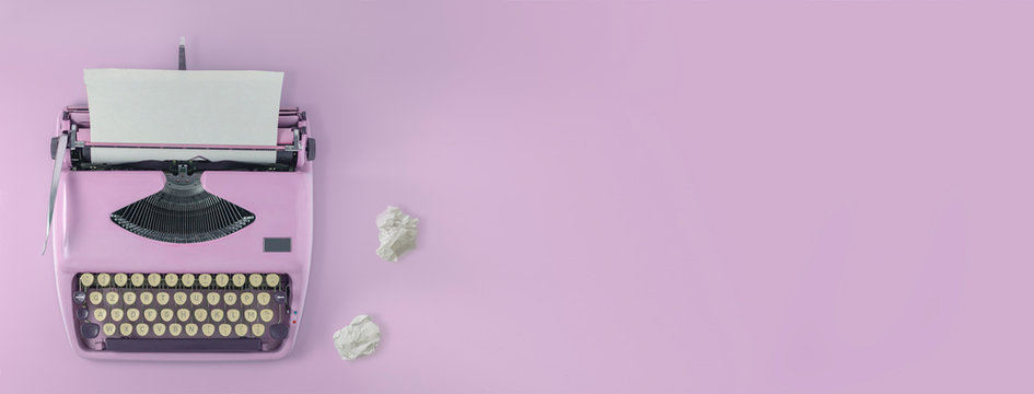 A pink vintage typewriter with pink background and two paper balls. 