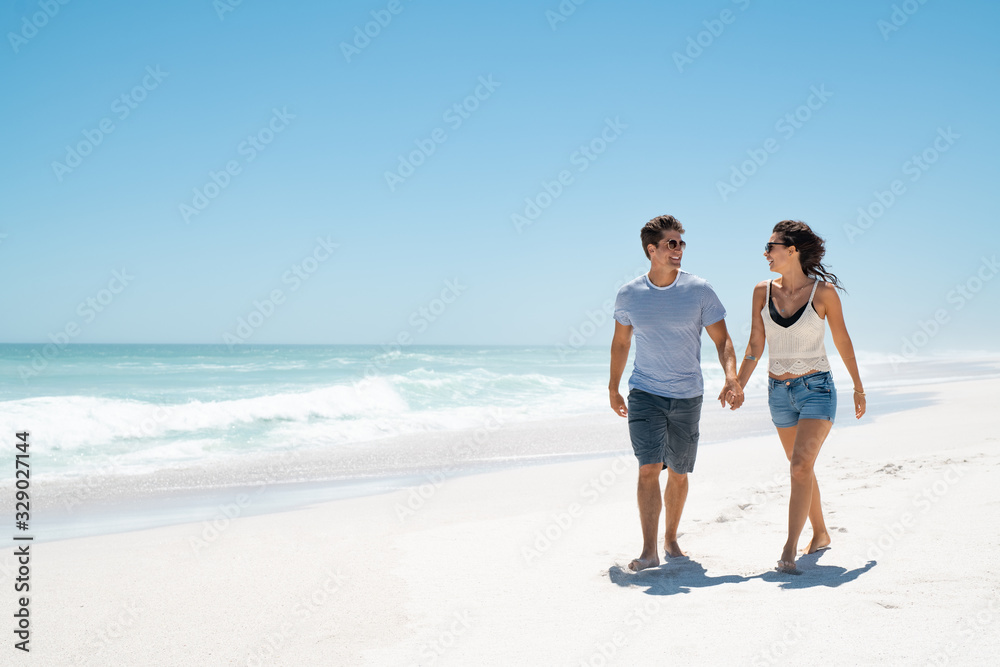 Young happy couple walking on beach - obrazy, fototapety, plakaty 