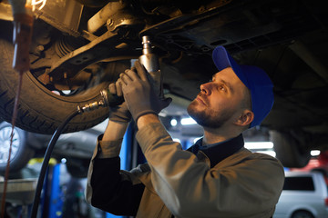 Horizontal medium close up shot of mature Caucasian repairman with beard in face working under car