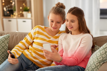 Wall Mural - people, technology and friendship concept - happy teenage girls with smartphones sitting on sofa at home