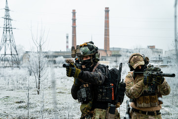 Wall Mural - Men in camouflage cloth and black uniform with machineguns side to side with factory on background. Soldiers with muchinegun aims aiming