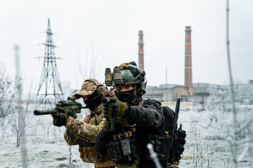 Wall Mural - Men in camouflage cloth and black uniform with machineguns side to side with factory on background. Soldiers with muchinegun aims aiming