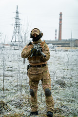 Wall Mural - Man in camouflage uniform hold machinegun. Soldier in the winter with factory on background