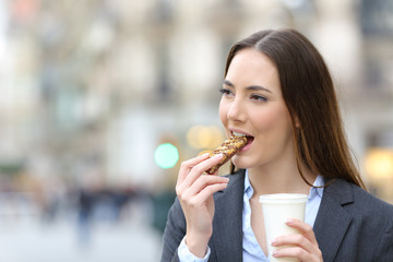 Business woman eating a snack bar holding a coffee