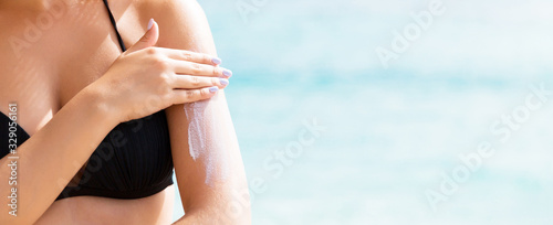 Sunscreen sunblock. Woman in a hat putting solar cream on shoulder outdoors under sunshine on beautiful summer day