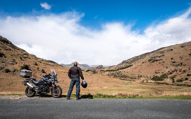 A motorcycle rider takes a break from his journey to appreciate the view in the English Lake District.