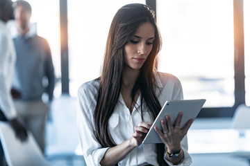 Concentrated young businesswoman using her digital tablet while standing in the coworking space.