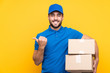 © luismolinero - Delivery man over isolated yellow background pointing to the side to present a product