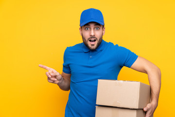 Wall Mural - Delivery man over isolated yellow background surprised and pointing finger to the side