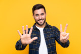 Fototapeta  - Young handsome man with beard over isolated yellow background counting seven with fingers