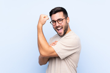 Wall Mural - Young handsome man with beard over isolated blue background making strong gesture