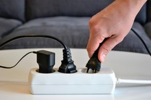 Male Hand Connecting An Electrical Plug To A Power Strip. Multi-socket Power Strip. Concept Of Electricity Savings, Increases, Costs