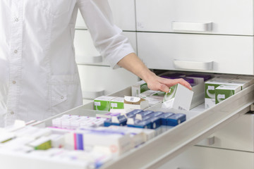 Pharmacist holding medicine box and capsule pack in pharmacy drugstore.