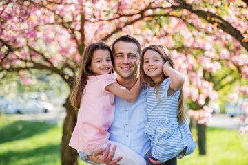 young father holding small daughters outside in spring nature.