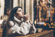 A young woman is sitting with her hands folded and is praying in a church