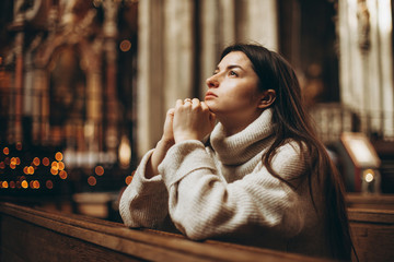 a young pretty woman came to the temple to pray to God. The parishioner of the church sits on a bench with her hands folded for prayer and heartily prays. copy space