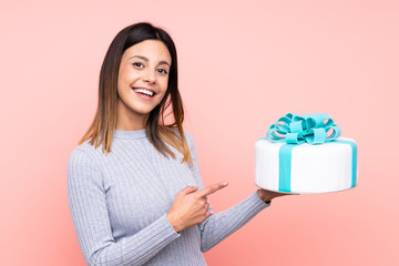 Wall Mural - Woman holding a big cake over isolated pink background and pointing it