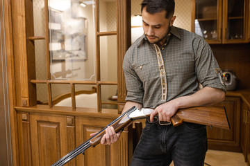 caucasian adult man reload a rifle for hunting in store, he stand with weapon around showcases. professional hunter keen on guns and firearm