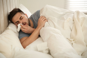 Wall Mural - Sick young man in bed at home. Influenza virus