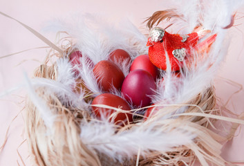 red, brown, purple Easter eggs in a nest with feathers and a bird on a beige