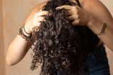 Young woman with long curly hair giving herself a scalp massage as part of her haircare routine