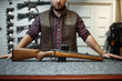 © Nomad_Soul - Man with rifle standing at counter in gun shop