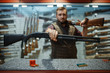 © Nomad_Soul - Man with two rifles at counter in gun shop