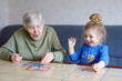 © Irina Schmidt - Beautiful toddler girl and grand grandmother playing together pictures lotto table cards game at home. Cute child and senior woman having fun together. Happy family indoors