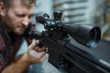 © Nomad_Soul - Man checks optical sight on sniper rifle, gun shop