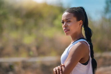 Outdoors portrait of beautiful African Female athlete standing with arms crossed against nature background.