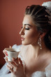 The bride in a lace veil drinks coffee on her wedding day. Fashion, beauty, style. Morning of the bride. Young beautiful bride with a cup of coffee waiting for her groom
