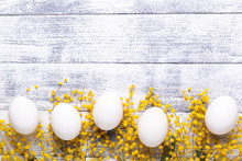 White Eggs, Yellow Mimosa Flowers On A Wooden Table. Easter Background