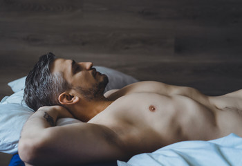 sexy naked young man stretching his hands and smiling while lying in bed. tattooed man