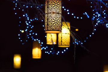 Evening street decor. Blue garlands and yellow lamps glowing on tree branches at night