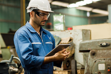 Wall Mural - Maintenance engineer industrial plant with a tablet in hand and document plan, Engineer looking of working at industrial machinery setup in factory.